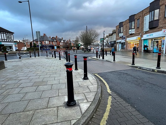 A level pedestrian crossing with black bollards on either side of the road