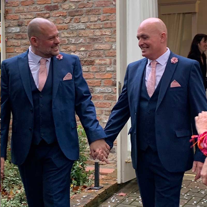 Two grooms leaving York Register Office holding hands and smiling happily