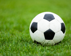 A black-and-white soccer ball rests on bright green grass in a sunlit field, creating a calm, fresh sports scene.