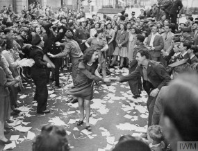 VE day celebrations, girl and boy dancing surrounded by a crowd throwing paper