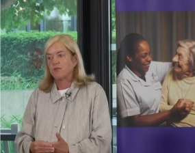 A woman stands next to a poster showing a carer and older resident
