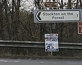 An official road signpost and an unauthorised poster below it