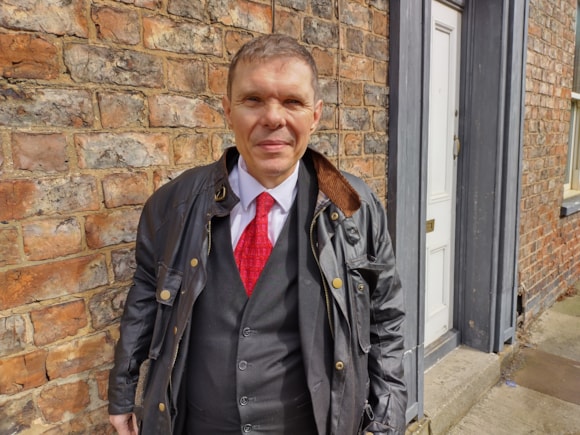 Man wearing a red tie stands in front of a brick wall