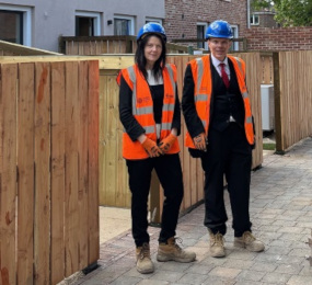 Two people in hard hats and hi-vis stand on newly-laid paving by new fencing