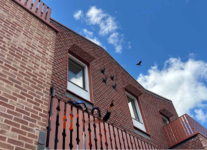 Two people stand on a decorative balcony of a brick and tile home
