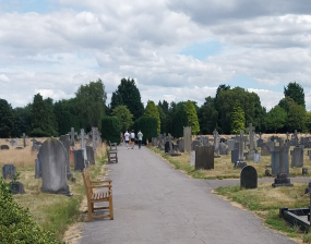 A burial ground with memorials, and a bench-lined path leading towards some trees.