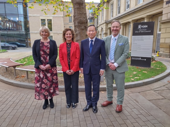 Two women and two men stand in front of stone building and a tree trunk