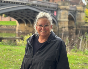 A photo of a woman smiling with a bridge behind her