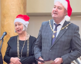A man and woman in Christmas hats sing
