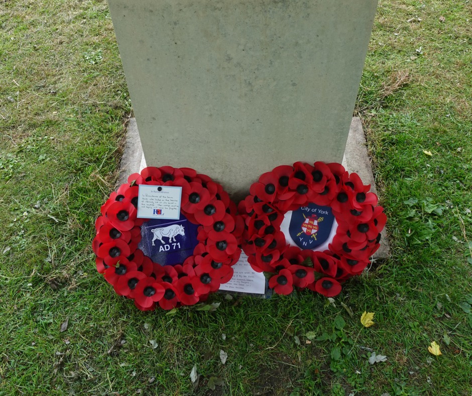 A stone memorial with two poppy wreaths laid against it