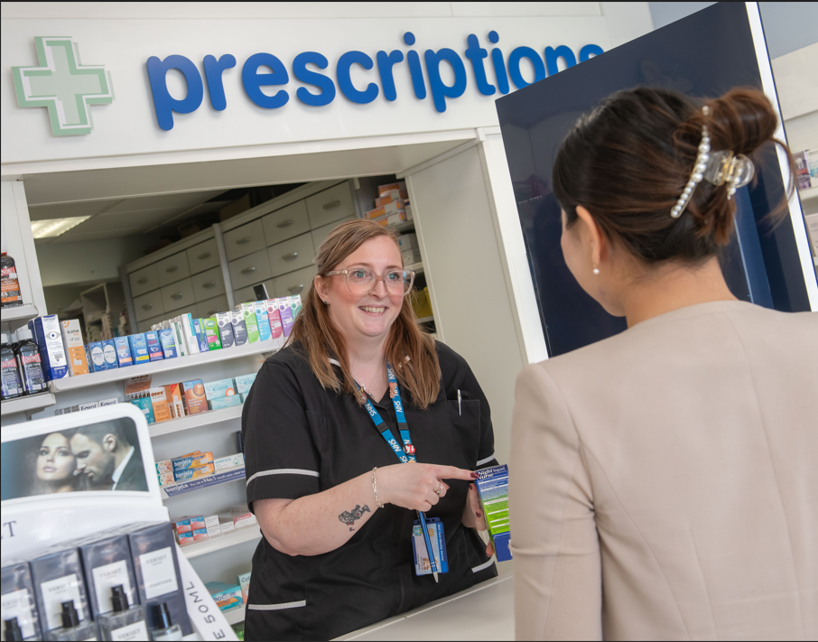 Image of a pharmacy worker behind a counter talking to a customer.