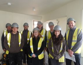 A group of people in a bare room smiling and wearing hi vis vests and headwear