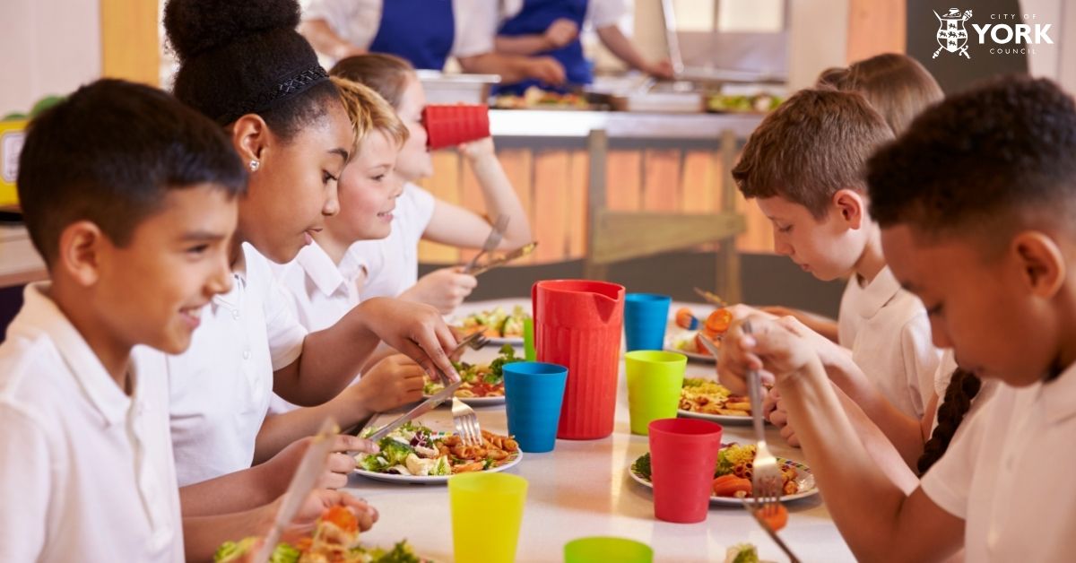 Image of school pupils sat eating their lunches at a long table
