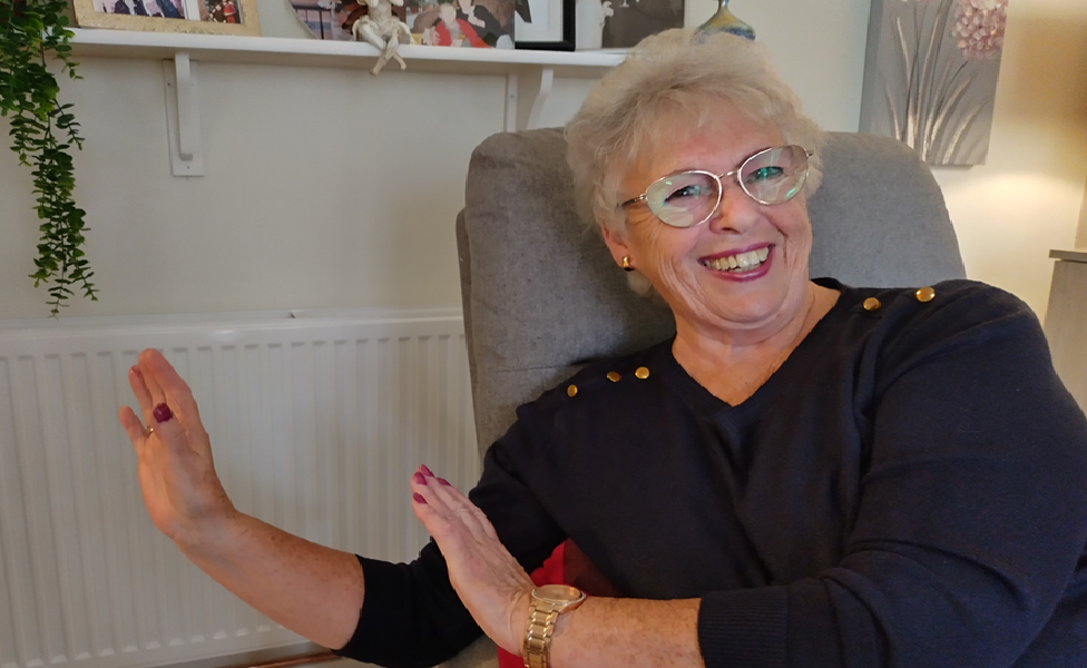 A smiling, seated woman warms her hands on a new radiator