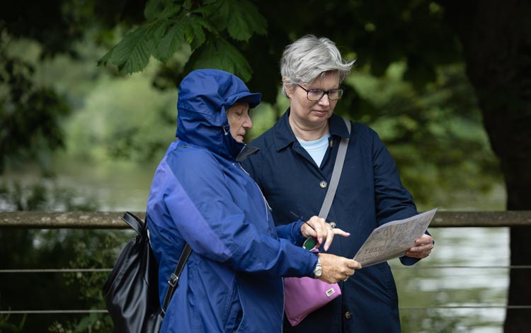 Two people walking along a riverside path, looking at a printed map.