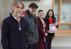 Two men and two women line up next to a poster