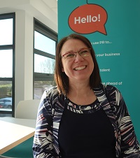 Monica, from Partner PR in front of a teal banner smiling.