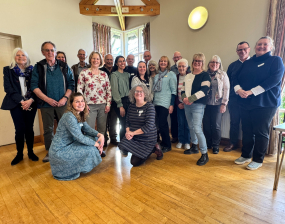 a group of people smiling towards the camera in a village hall