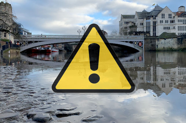 Lendal Bridge from the River Ouse, showing raised river levels; a yellow warning triangle icon overlays the photograph.