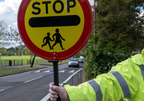School crossing patroller sign which is a yellow circle outlined by red with the word stop in the centre and the image of two children walking