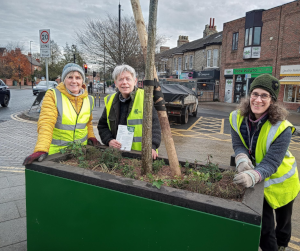 3 volunteers stand smiling around a new planter whilst wearing yellow high-vis jackets