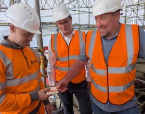 Three men in high vis jackets stand on the scaffolding surrounding Bootham Bar and examine the items.