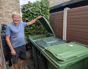 A man stands next to a row of green bins smiling and looking happy