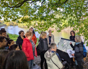A group of people stand next to a river in York listening to a speaker