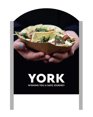 A 'Make It York' welcome sign with a woman holding some food in the background.