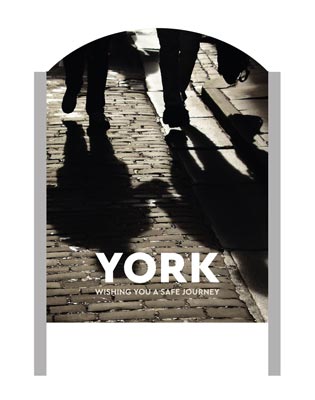 A 'Make It York' welcome sign with some shadows of people on a cobbled street in the background.