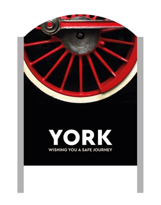 A 'Make It York' welcome sign with a steam train wheel in the background.
