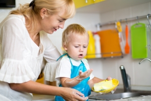 A woman helps a young child to wash dishes.