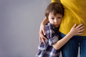 A sad looking child hugs an adult.