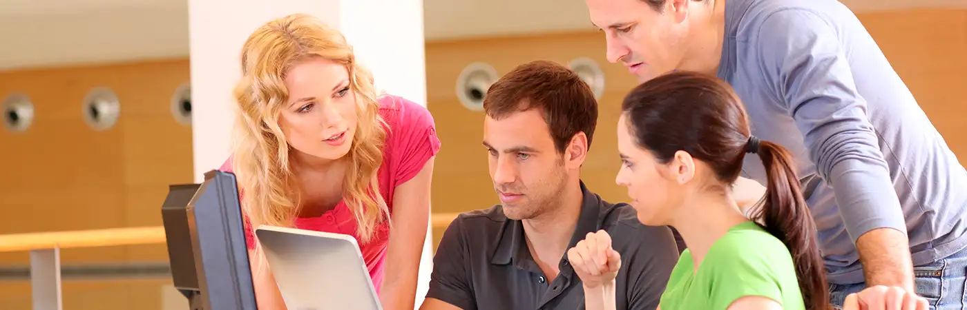 A group of young people crowd around a tablet PC held by a young woman.